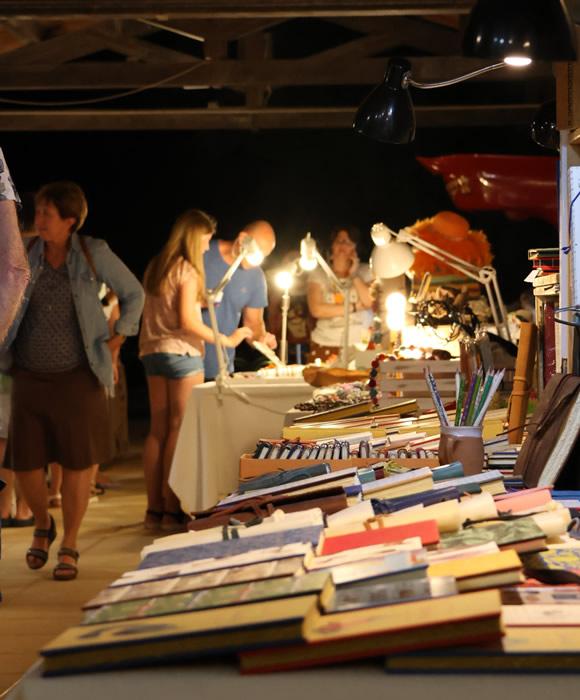 Mercatino serale vivace, libri colorati e persone curiose sotto luci calde.
