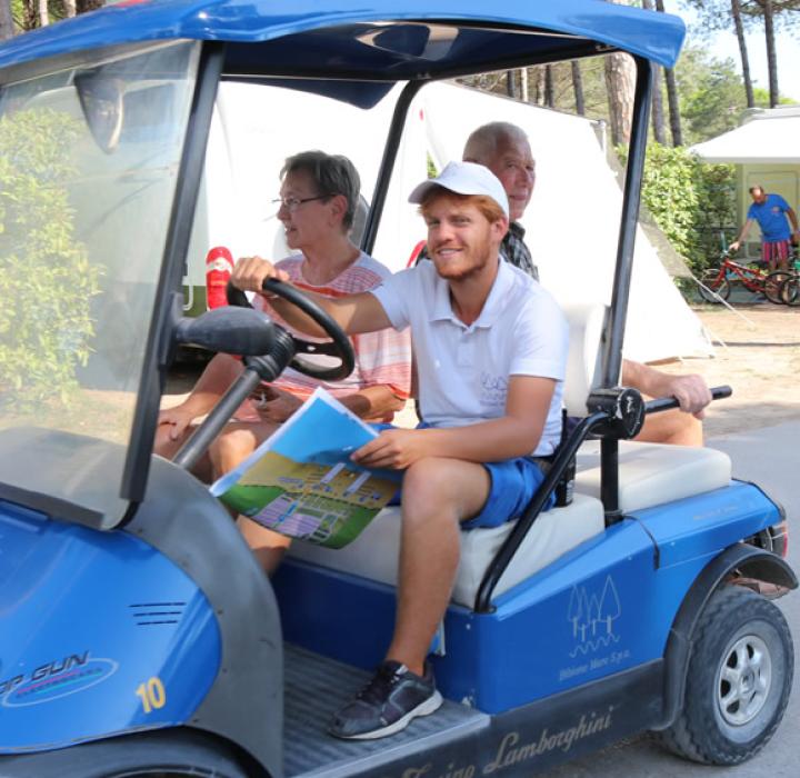 Happy people on a blue golf cart in a sunny campsite.